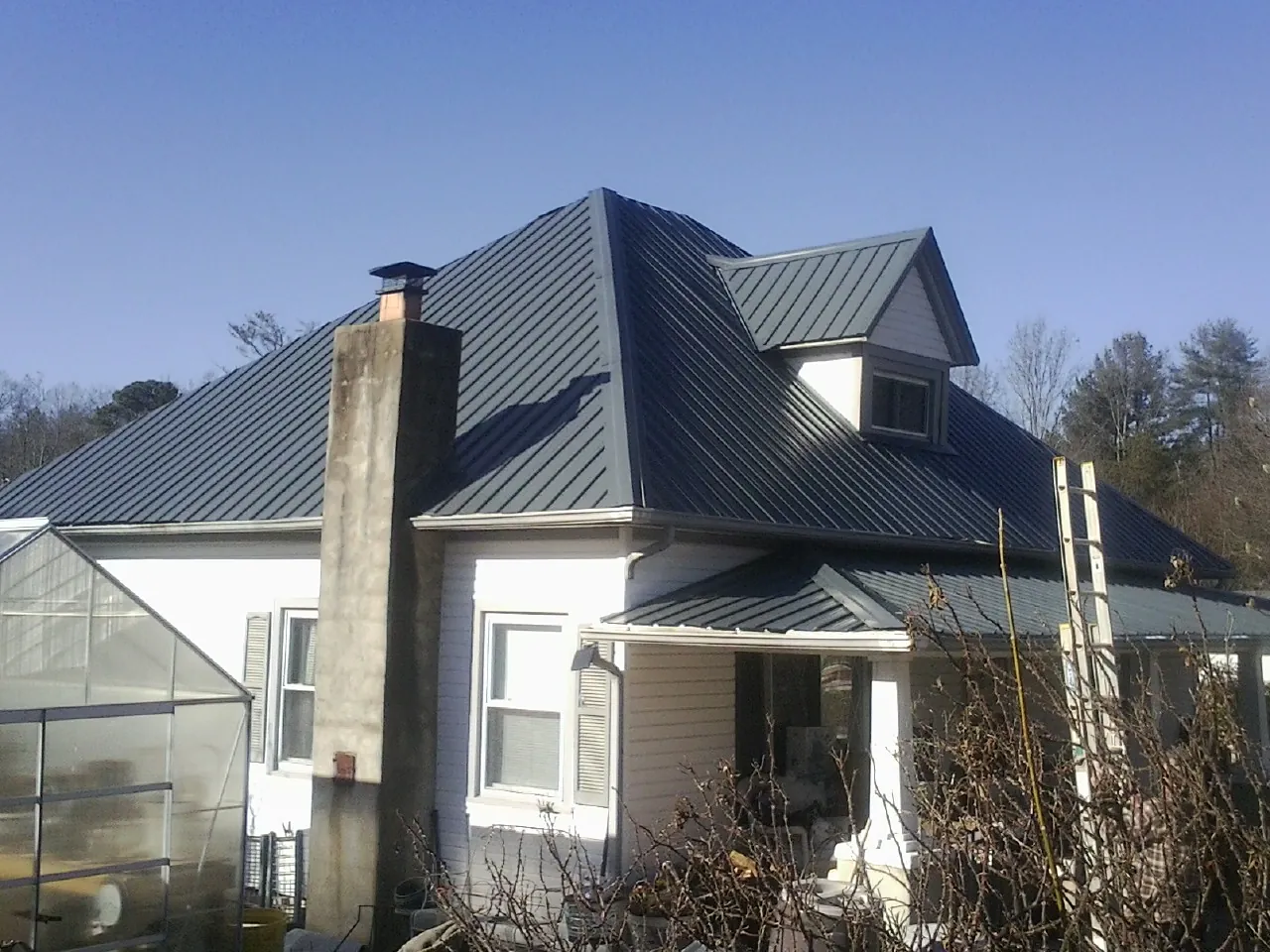 Dark blue standing seam metal roof on a white farmhouse with dormer — Slate & Tile Roof Repair by Roofing Brothers in Humeston