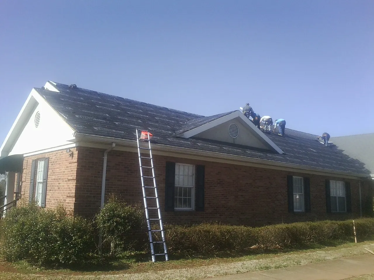 Crew tearing shingles off a brick ranch roof with a ladder set — Emergency Roof Repair work by our crew in Humeston