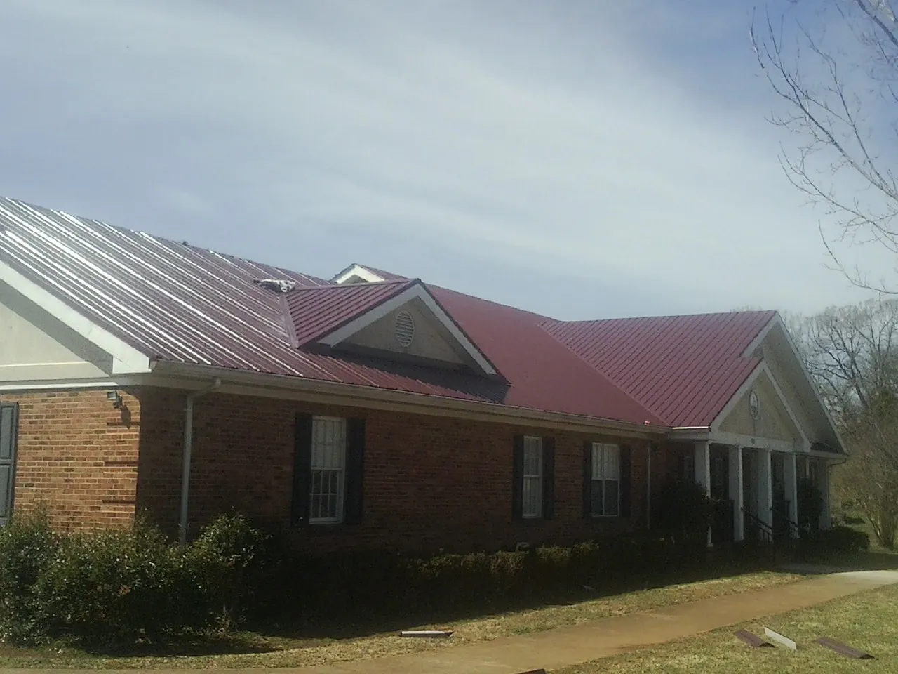 Red metal roof with gabled entries on a long brick building, from a Hail Damage Roof Repair job in Humeston