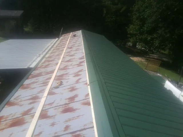 Old rusted panels beside newly installed green metal roofing — Wind Damage Roof Repair by Roofing Brothers in Humeston