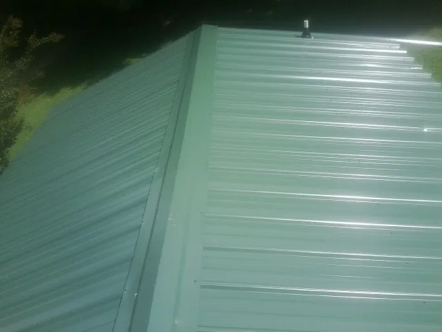 New green metal panels meeting at the ridge of a roof — Flat Roof Repair work by our crew in Humeston