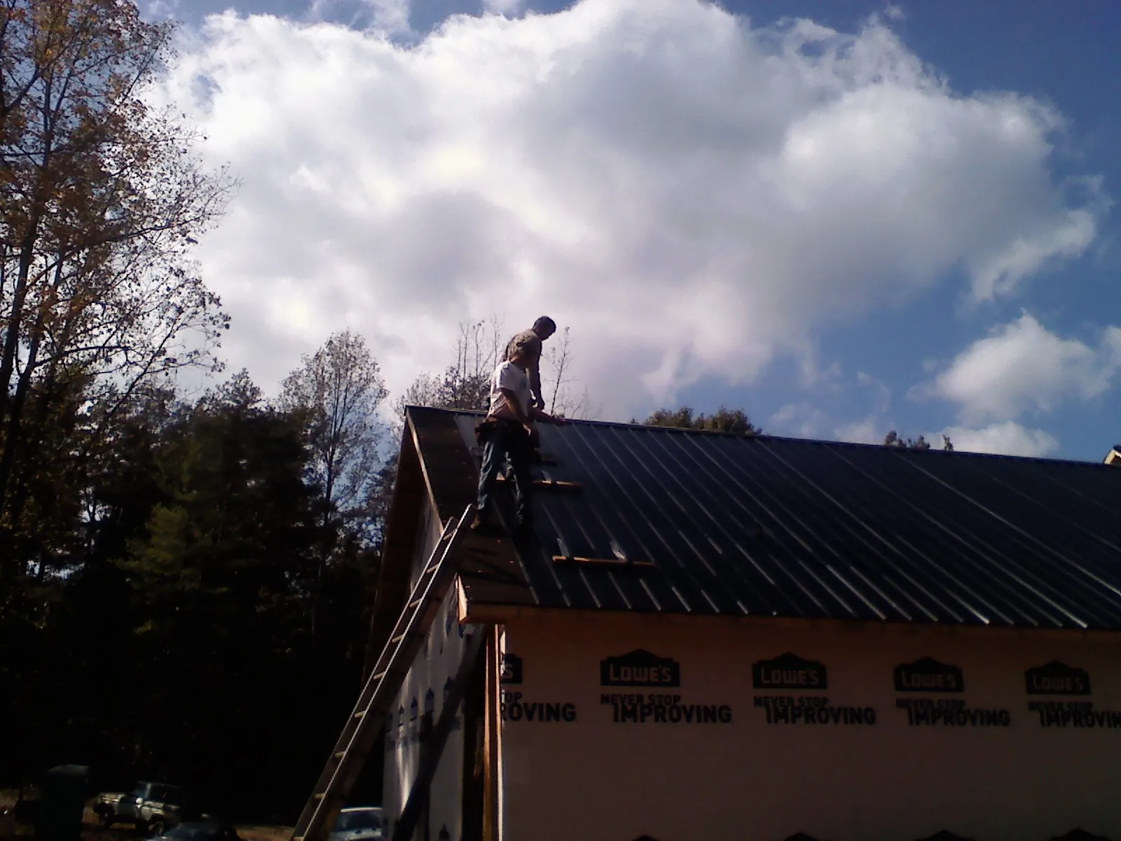 Roofer fastening dark metal panels high against a cloudy sky, from a Roof Inspection job in Humeston