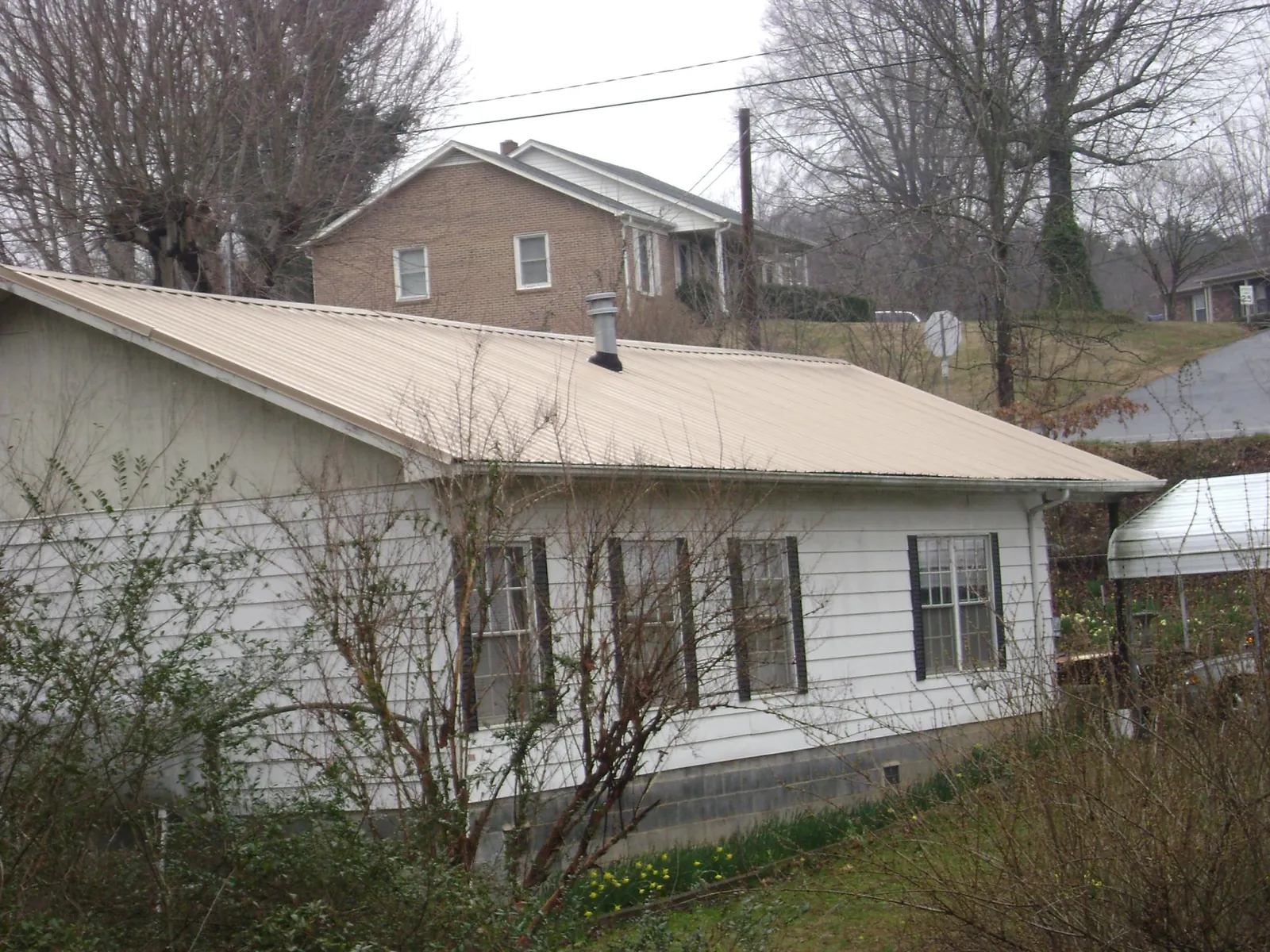 Tan metal roof on a white sided house set into a hillside — Commercial Roofing by Roofing Brothers in Humeston