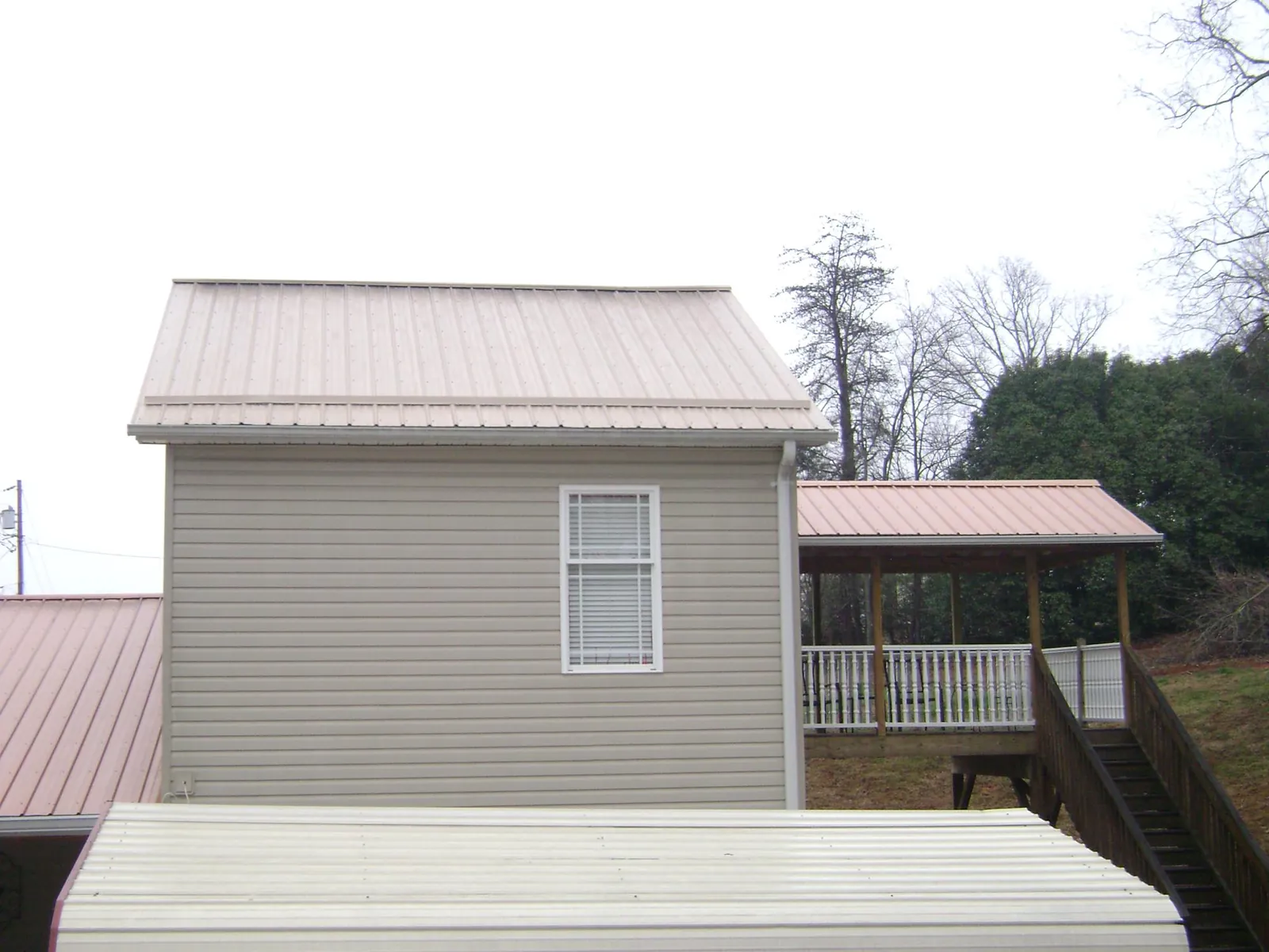 Tan metal roofs on a two story addition and attached porch, from a Roof Replacement job in Humeston